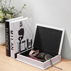 an open book with sunglasses and other items in it sitting on a table next to a flower pot