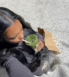 a woman sitting on the ground drinking from a green cup with a straw in her mouth