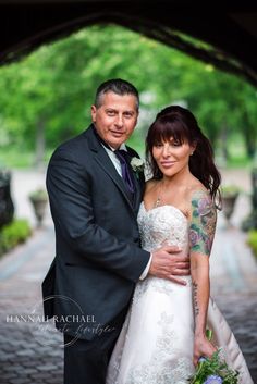 a bride and groom pose for a wedding photo under an arch in the city park