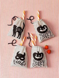 four halloween treat bags with candy sticks in them on a pink and white striped tablecloth