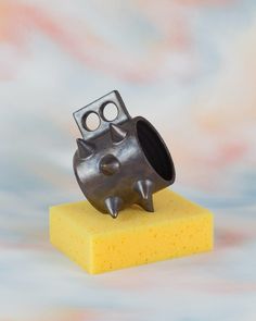 a small metal object sitting on top of a yellow block of waxy paper with holes in the middle