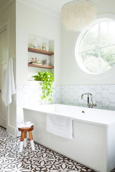 a white bath tub sitting under a window next to a wooden stool in a bathroom