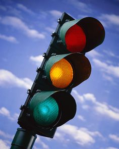 a traffic light that is red and green against a blue sky with clouds in the background