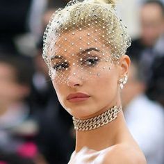 a woman in a white dress with pearls on her head and veil over her face