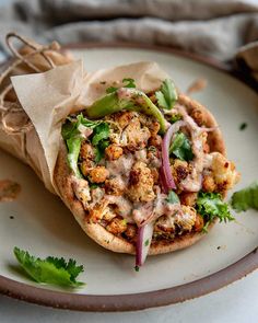 a pita sandwich with meat and vegetables on a white plate next to cilantro