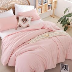 a bed with pink sheets and pillows in a bedroom next to a plant on the floor