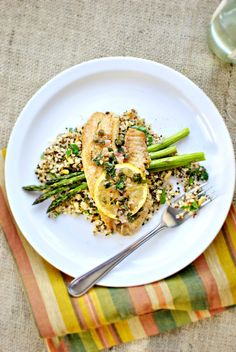 a white plate topped with chicken and asparagus next to a glass of water