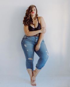 a woman in ripped jeans leaning against a wall with her hands on her hips and looking at the camera