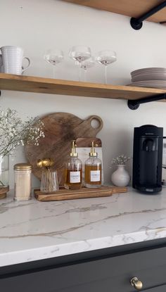 a kitchen counter topped with lots of bottles and glasses next to a wooden cutting board