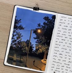 an open book with writing on it sitting on top of a wooden table next to a lamp post