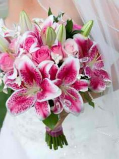 a bride holding a bouquet of pink and white lilies in her hand, while wearing a veil