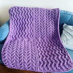 a purple knitted blanket sitting on top of a blue couch next to a pillow