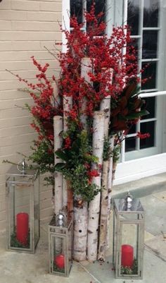 some red candles are sitting next to white birch trees and branches with red flowers in them