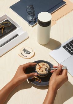 a person holding a bowl of food in front of a laptop computer on a desk