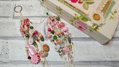 two pairs of pink and green earrings hanging from hooks on a brick wall next to a box