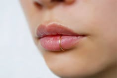 a woman's nose with a gold ring on her lip and the tip of her tongue sticking out