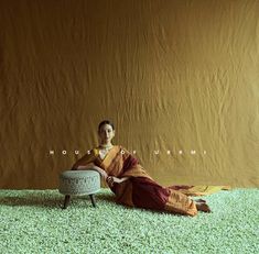 a woman sitting on top of a white ottoman in front of a brown wall and green carpet