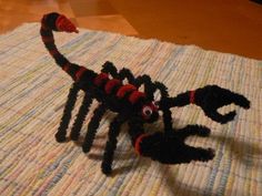 a toy scorpion is sitting on top of a tablecloth covered with strips of yarn