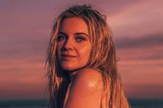 a woman standing on the beach at sunset with her hair blowing in the wind and looking off into the distance