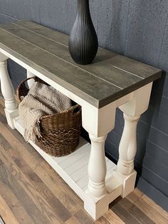 a white table with a basket under it and a black vase on the end shelf