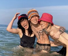 three women are posing in the water with their arms around each other while wearing hats