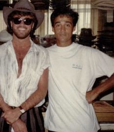 two men standing next to each other in front of a window wearing hats and sunglasses