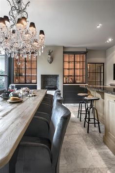 a long wooden table sitting under a chandelier next to a bar with stools