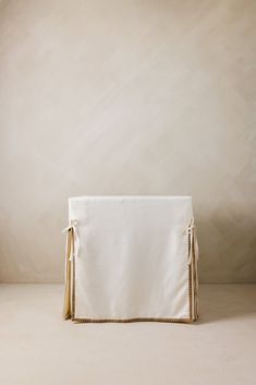 a white and gold clutch bag with tassels on the front, sitting against a beige wall