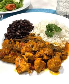 a white plate topped with rice and meat covered in sauce next to black beans on a table