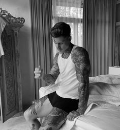 a tattooed man sitting on top of a bed