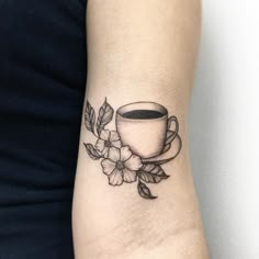 a woman's arm with a cup of coffee and flowers tattoo on the wrist