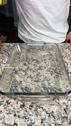 a glass dish sitting on top of a counter next to a person in a white t - shirt