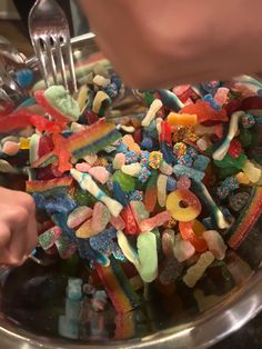 a bowl filled with lots of different colored candies next to a person holding a fork