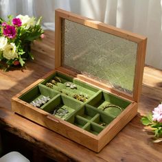 a wooden box filled with jewelry sitting on top of a table next to some flowers