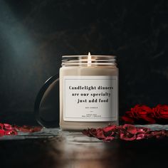 a candle sitting on top of a wooden table next to red rose petals and roses