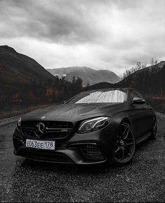 a black car parked on the side of a road in front of mountains and trees