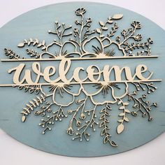 a wooden sign that says welcome with flowers and leaves in the center on a blue background