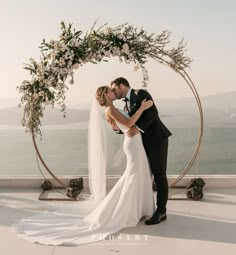 a bride and groom kissing in front of an arch decorated with flowers