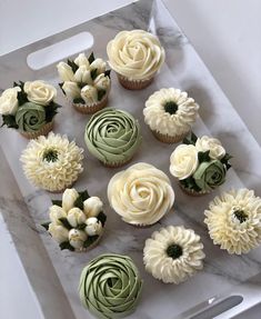 cupcakes decorated with white and green icing on a marble tray next to a knife