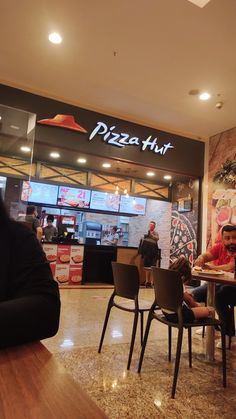 people sitting at tables in front of a pizza hut with an advertisement on the wall