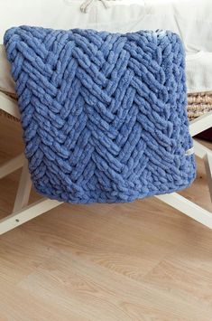 a blue knitted pillow sitting on top of a wooden floor next to a bed