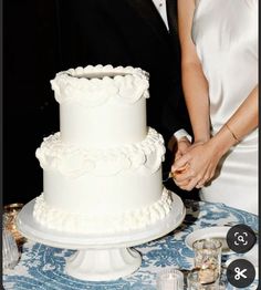 a newly married couple cutting their wedding cake at the reception table with white frosting