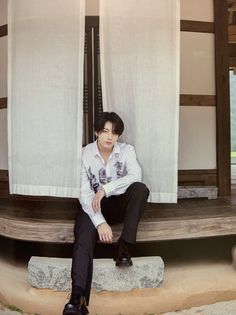 a man sitting on top of a stone bench next to a white curtained wall