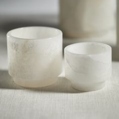 two white bowls sitting next to each other on top of a cloth covered tablecloth