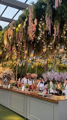 a group of people standing at a counter with flowers hanging from the ceiling behind them