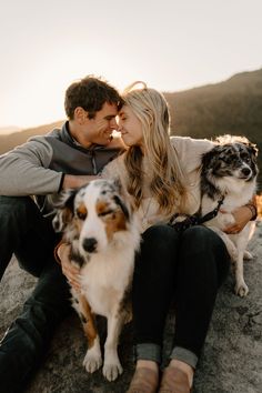 a man and woman sitting on top of a rock with two dogs next to them