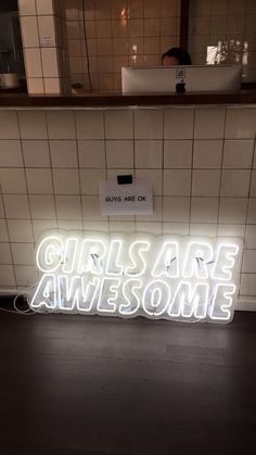 a neon sign that says girls are awesome in front of a white tiled bathroom wall