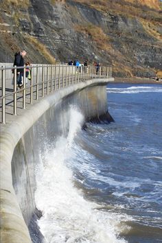 people are standing on the edge of a dam wall as waves crash into the water