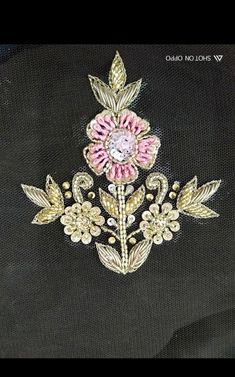 a pink and gold brooch sitting on top of a piece of cloth next to a black background