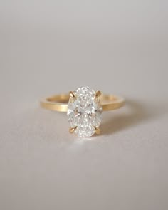 an oval cut diamond sits on top of a plain gold band, with the center stone set in yellow gold